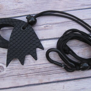 May include: Black leather key chain with a black cord, a black carabiner clip, and two black beads. The leather piece is shaped like a bat wing with a textured surface.