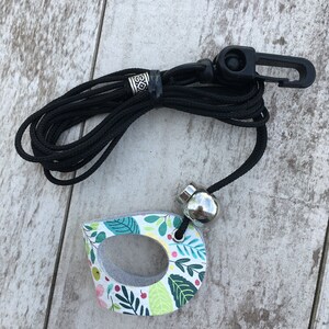 May include: A black lanyard with a silver bead and a floral patterned wooden charm. The charm has a hole in the center and is shaped like a teardrop.