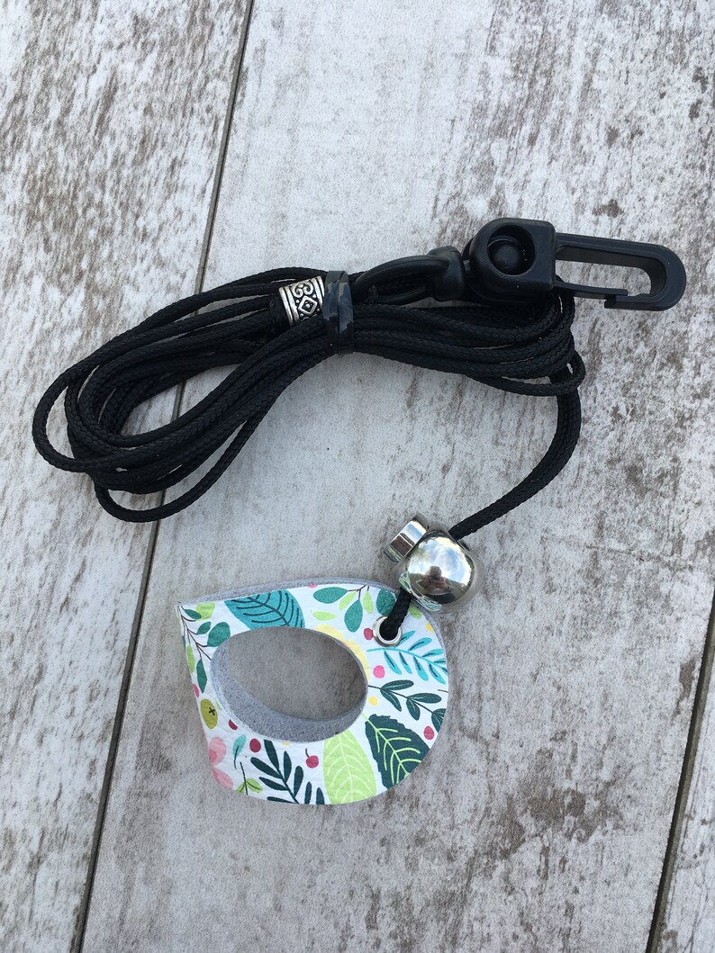 May include: A black lanyard with a silver bead and a floral patterned wooden charm. The charm has a hole in the center and is shaped like a teardrop.
