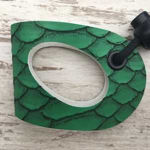 May include: Green paddleboard handle with a textured, scaly surface and a black cord with a round black stopper.