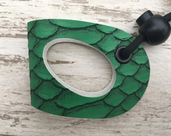 May include: Green paddleboard handle with a textured, scaly surface and a black cord with a round black stopper.