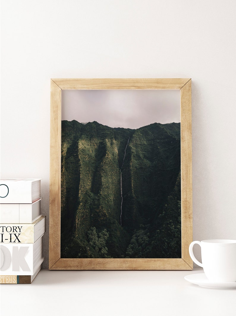 May include: A framed photograph of a lush green mountain range with a waterfall cascading down the side. The photograph is in a light brown wooden frame.