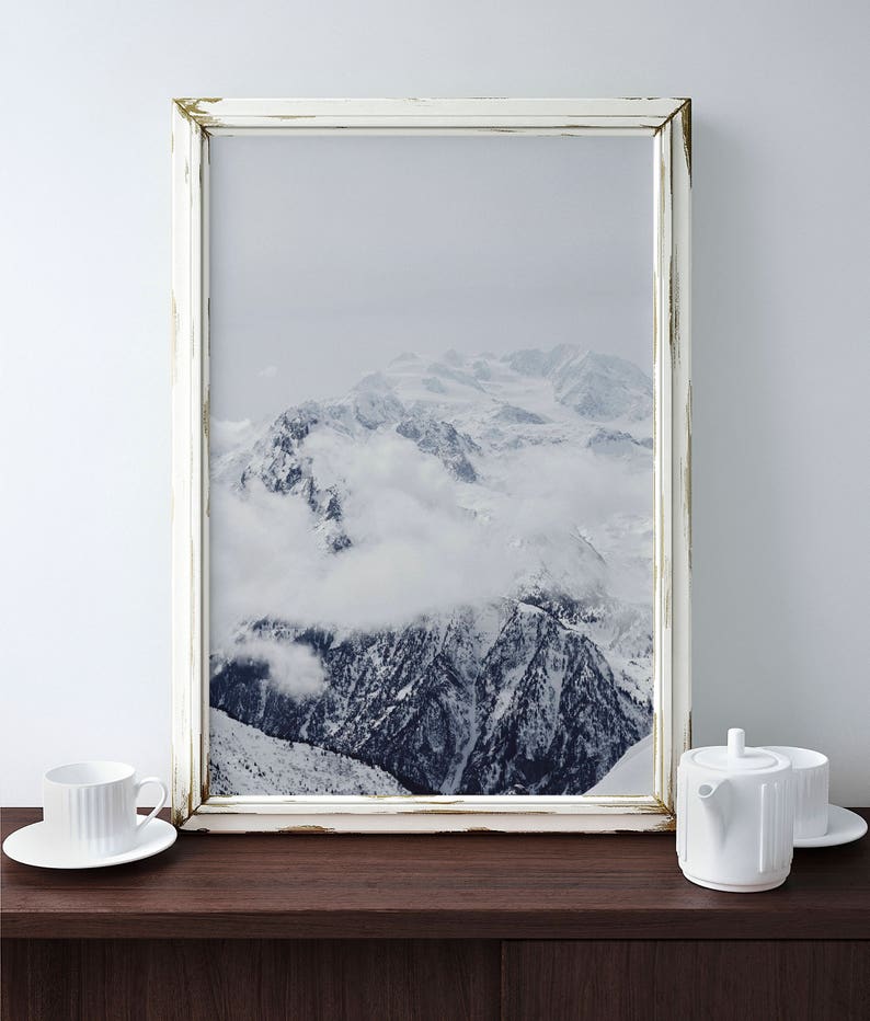 Peut inclure: Une photographie encadr&eacute;e en blanc d'une cha&icirc;ne de montagnes enneig&eacute;es avec des nuages ​​couvrant les sommets. Le cadre a une finition blanche vieillie.