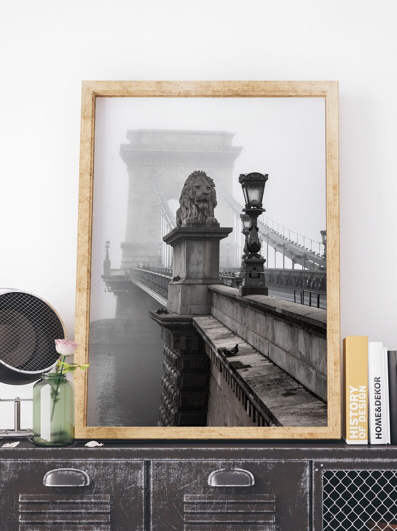 May include: A black and white photograph of a bridge with a lion statue on top of a pillar. The bridge is covered in fog and the photo is framed in a wooden frame.