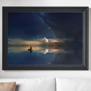 May include: A framed print of a sailboat sailing on a calm body of water under a starry night sky. The Milky Way is visible in the sky, and the water reflects the stars and clouds.