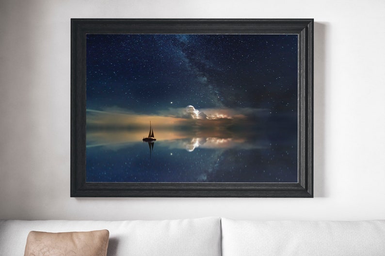 May include: A framed print of a sailboat sailing on a calm body of water under a starry night sky. The Milky Way is visible in the sky, and the water reflects the stars and clouds.
