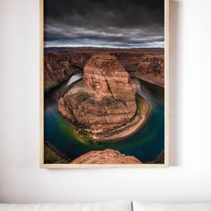 Puede incluir: Fotograf&iacute;a enmarcada de Horseshoe Bend, Arizona. La imagen captura la ic&oacute;nica curva en forma de herradura del r&iacute;o Colorado, con formaciones rocosas rojas y un cielo oscuro y nublado. El agua es de un azul verdoso profundo.