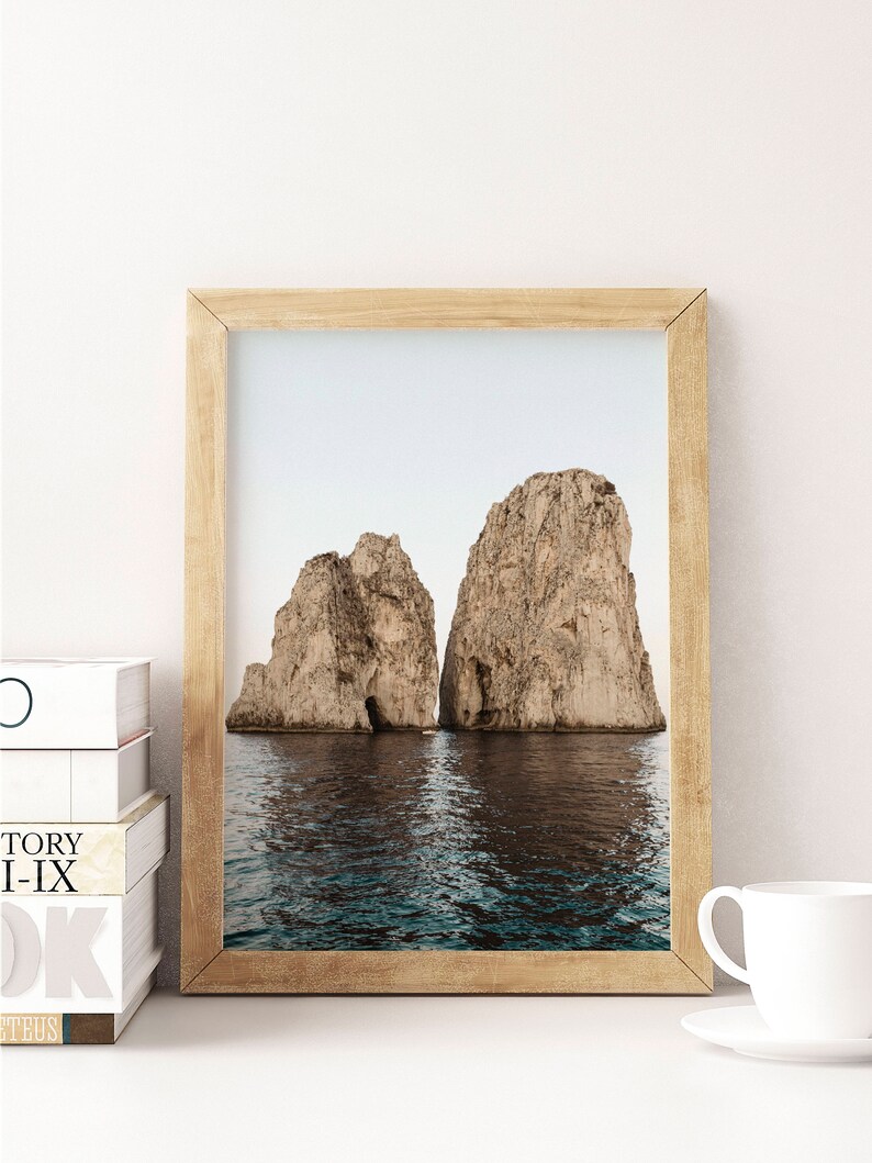 May include: A framed photograph of two large rock formations rising out of the ocean. The water is a deep blue and the sky is a light blue. The rocks are a light brown color.