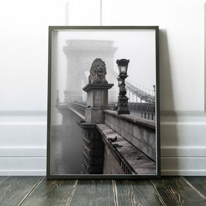 May include: A black and white photograph of a bridge with a lion statue on top of a pillar. The bridge is covered in fog and there is a street lamp on the side of the bridge.