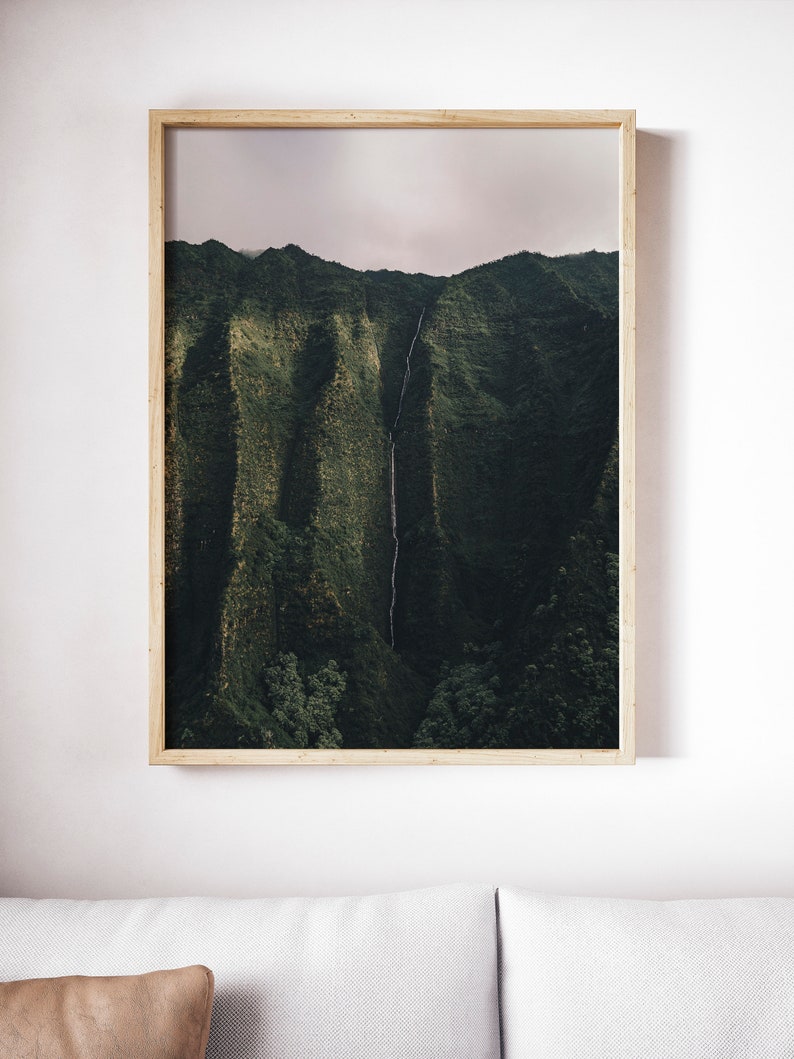 May include: A framed photograph of a lush green mountain range with a waterfall cascading down the side. The sky is a soft, light pink.