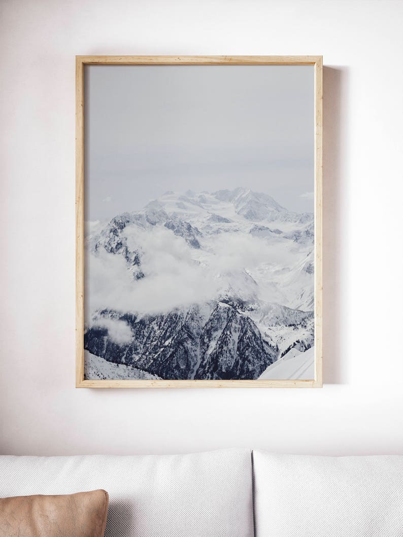 Peut inclure: Une photographie encadr&eacute;e d'une cha&icirc;ne de montagnes enneig&eacute;es avec des nuages ​​couvrant les sommets. Les montagnes sont recouvertes de neige et le ciel est bleu clair.