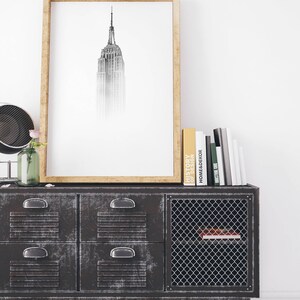 Peut inclure: Une impression en noir et blanc encadr&eacute;e de l'Empire State Building, suspendue au-dessus d'une armoire en m&eacute;tal noir avec quatre tiroirs et une porte en grillage m&eacute;tallique. L'armoire a une &eacute;tag&egrave;re &agrave; l'int&eacute;rieur de la porte. Plusieurs livres sont empil&eacute;s sur le dessus de l'armoire.