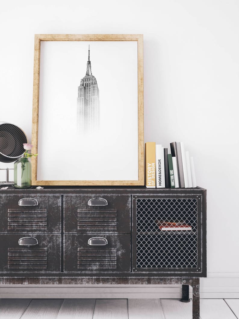 Peut inclure: Une impression en noir et blanc encadr&eacute;e de l'Empire State Building, suspendue au-dessus d'une armoire en m&eacute;tal noir avec quatre tiroirs et une porte en grillage m&eacute;tallique. L'armoire a une &eacute;tag&egrave;re &agrave; l'int&eacute;rieur de la porte. Plusieurs livres sont empil&eacute;s sur le dessus de l'armoire.