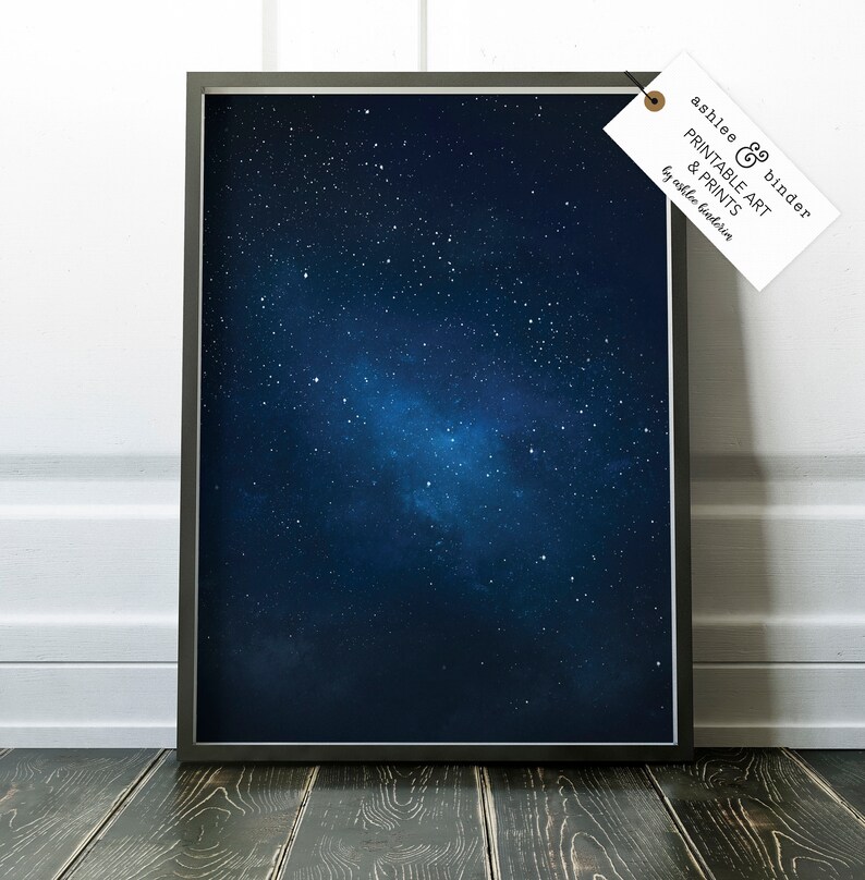 K&ouml;nnte beinhalten: Ein gerahmter Druck eines dunkelblauen Nachthimmels mit einem Haufen wei&szlig;er Sterne und einem schwachen Nebel. Der Druck ist in einem schwarzen Rahmen und hat ein wei&szlig;es Etikett mit dem Text "Ashlee & Binder Printable Art & Prints by Ashlee Binder".