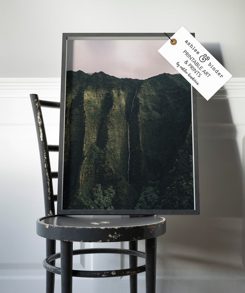 May include: A framed photograph of a lush green mountain range with a waterfall cascading down the side. The photograph is in a black frame and is sitting on a black wooden chair.