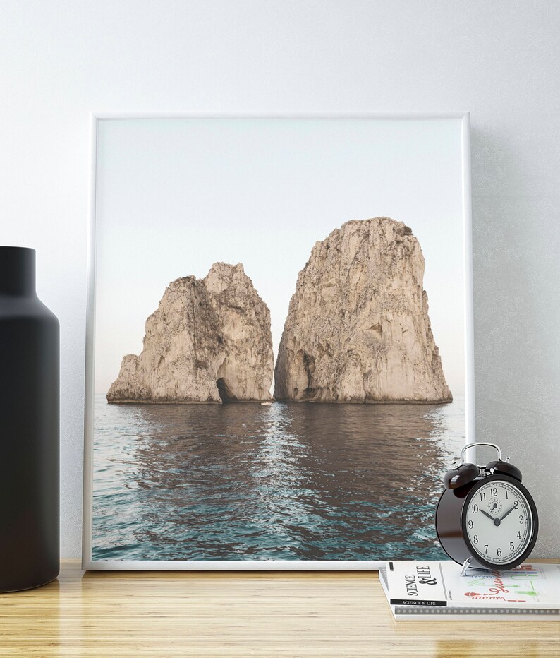 May include: A framed photograph of two large rock formations rising out of the ocean. The water is a light blue and the sky is a pale gray. The rocks are a light brown color.