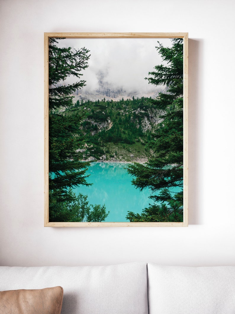 Op de afbeelding: Een ingelijste foto van een bergmeer omringd door bomen. Het meer is een levendige turquoise blauw en de bergen zijn bedekt met mist. De bomen zijn groen en omlijsten het meer.