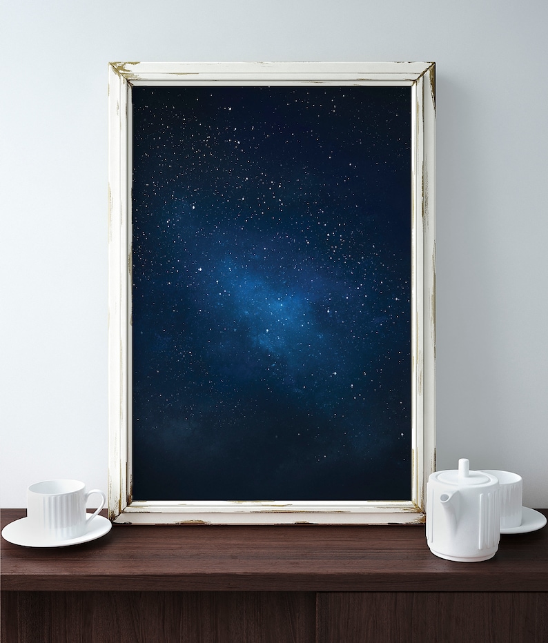 K&ouml;nnte beinhalten: Ein wei&szlig; gerahmtes Bild mit einem dunkelblauen Hintergrund und wei&szlig;en Sternen. Das Bild steht auf einer dunkelbraunen Holzoberfl&auml;che mit einer wei&szlig;en Teetasse und einer wei&szlig;en Teekanne.