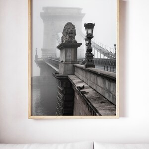 May include: A black and white photograph of a bridge with a lion statue on top. The bridge is covered in fog and there is a street lamp on the side of the bridge.
