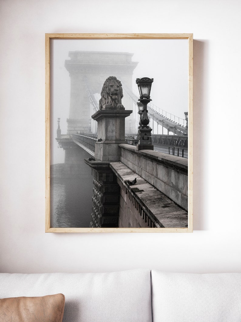 May include: A black and white photograph of a bridge with a lion statue on top. The bridge is covered in fog and there is a street lamp on the side of the bridge.