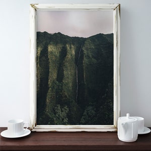 May include: A white framed photograph of a lush green mountain range with a waterfall cascading down the side. The frame has a distressed white finish.