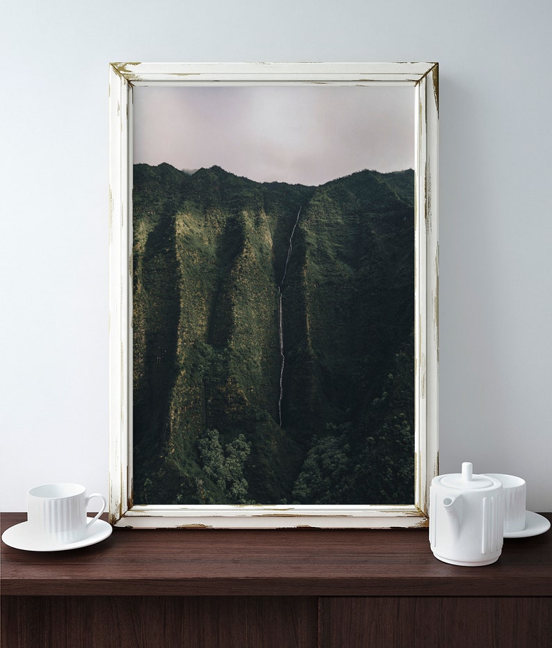 May include: A white framed photograph of a lush green mountain range with a waterfall cascading down the side. The frame has a distressed white finish.