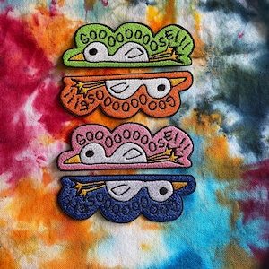 May include: Four embroidered iron-on patches featuring a cartoon goose with the text "GOOOOOSE!" in a cloud shape. The patches are in green, orange, pink, and blue.