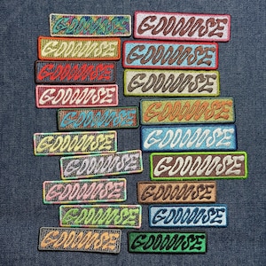 May include: A collection of rectangular embroidered patches, each featuring the word GOOOOOSE in a stylized, wavy font. The patches come in a variety of vibrant color combinations, including red, blue, green, yellow, and brown, with contrasting thread.