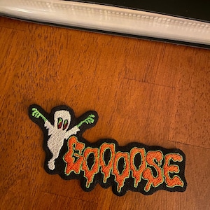 May include: A black and green embroidered patch with a white ghost and the word "Boo-oose" in orange letters.