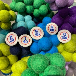 May include: A close-up of a variety of colorful felt balls with white circles attached to them. The circles have letters and numbers on them, spelling out the word "Bingo" and the numbers 20, 40, 60, 80, and 100.