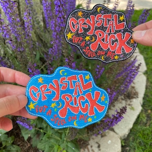 Peut inclure: Deux patchs brodés en forme de nuage. Le patch du haut est noir avec du texte rouge qui dit "Crystal Rick" et "Put a Spell on Me". Le patch du bas est bleu avec du texte rouge qui dit "Crystal Rick" et "Put a Spell on Me".