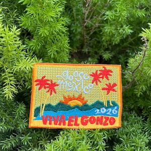 May include: Embroidered patch with a tropical scene featuring palm trees, a sunset, and the text "Viva El Gonzo" in red. The patch also includes the text "dose mexico" and the year "2026". The patch has an orange border and is set against a backdrop of green foliage.