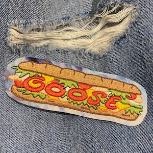May include: Embroidered patch featuring a cartoon submarine sandwich with the word "GOOSE" in red. The sandwich has lettuce, tomatoes, and cheese. The patch is on a blue denim background with a distressed area.