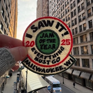 May include: Embroidered patch with the text "I SAW IT!" and "JAM OF THE YEAR 2025 EVERYTHING MUST GO MILWAUKEE, WI." The patch is circular with a red border and a green center.