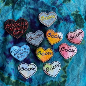May include: A collection of heart-shaped embroidered patches. Some patches feature the word "Goose", while others read "Goose is a Midwest Band". The patches are in various colors, including denim, black, blue, yellow, and pink.