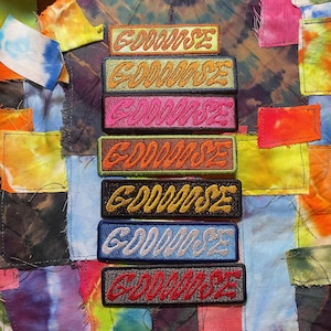 May include: Nine embroidered patches with the word "GOODWISE" in a variety of colors and fonts. The patches are arranged vertically on a colorful fabric background.