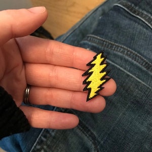 May include: Yellow lightning bolt patch with black outline. The patch is embroidered and has a textured surface.