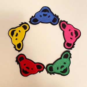 May include: Five colorful embroidered iron-on patches featuring a bear face design. The patches are in shades of blue, yellow, red, green, and pink.