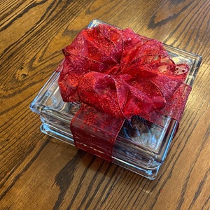 May include: A stack of clear glass coasters with a red glittery bow on top. The coasters are square and have a beveled edge.