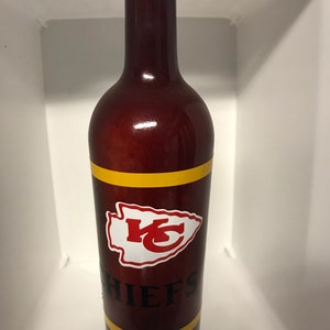May include: A brown glass wine bottle with a red, white, and gold Kansas City Chiefs logo and the word "CHIEFS" in black lettering.