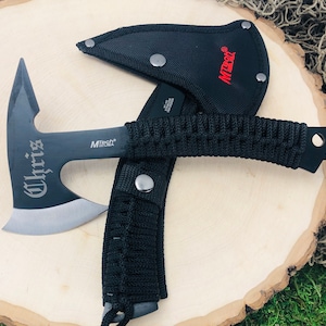 May include: Black tactical axe with a black nylon sheath and a black paracord handle. The axe blade is engraved with the word "Chris".