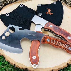 May include: Two axes with wooden handles and stainless steel blades are displayed. One axe has the name "LYNDSE" engraved on the handle. The axes are accompanied by black sheaths. The "Elk Ridge" logo is visible on the blades and sheaths.