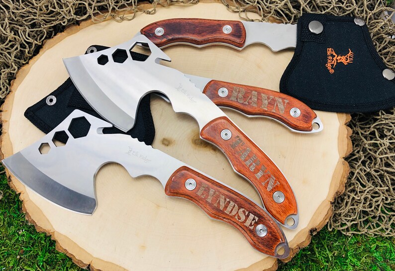 May include: A collection of hatchets with stainless steel blades and wooden handles. The hatchets have a hexagonal design on the blade and are engraved with names. One hatchet is in a black sheath with an orange logo.