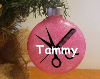 May include: Pink glitter Christmas ornament with a pair of scissors and a comb, and the name "Tammy" written on it.