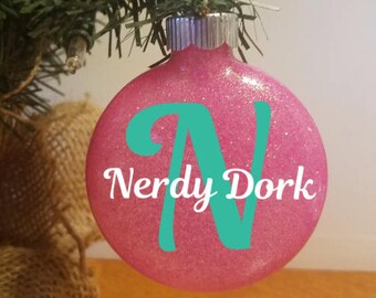 May include: Pink glitter Christmas ornament with a teal letter N and the text "Nerdy Dork".