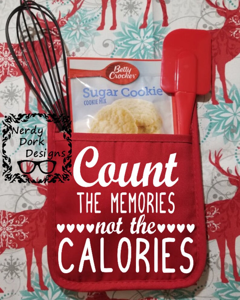 Op de afbeelding: Een rode ovenwant met de tekst "Count the memories not the calories" in wit. De ovenwant heeft een zakje met een garde, een spatel en een pakje suikerkoekmix.