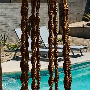 May include: A macrame plant hanger with a brown ceramic pot. The hanger is made of natural rope and has a tassel at the bottom. The pot is hanging over a swimming pool.