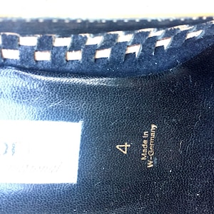 May include: Close-up of the inside of a black shoe with a white stitched trim. The shoe is labeled "4" and "Made in W-Germany".