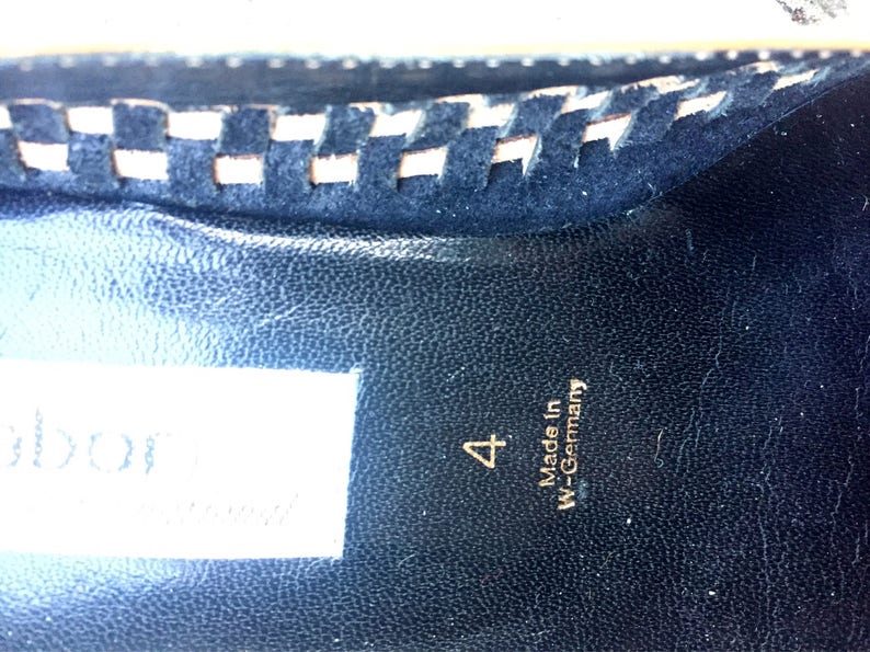 May include: Close-up of the inside of a black shoe with a white stitched trim. The shoe is labeled "4" and "Made in W-Germany".