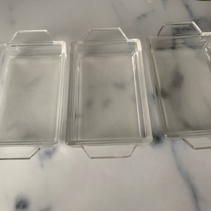 K&ouml;nnte beinhalten: Drei transparente Glasbackformen mit Griffen. Die Formen sind rechteckig und haben eine matte Oberfl&auml;che.